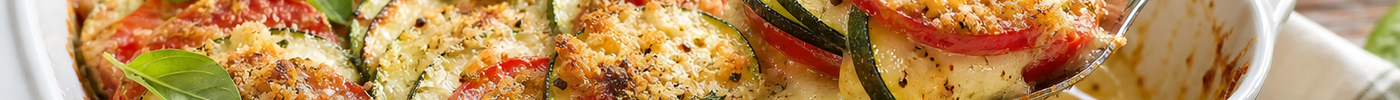 Baked summer tomato zucchini gratin with Parmesan and fresh basil in a white baking dish